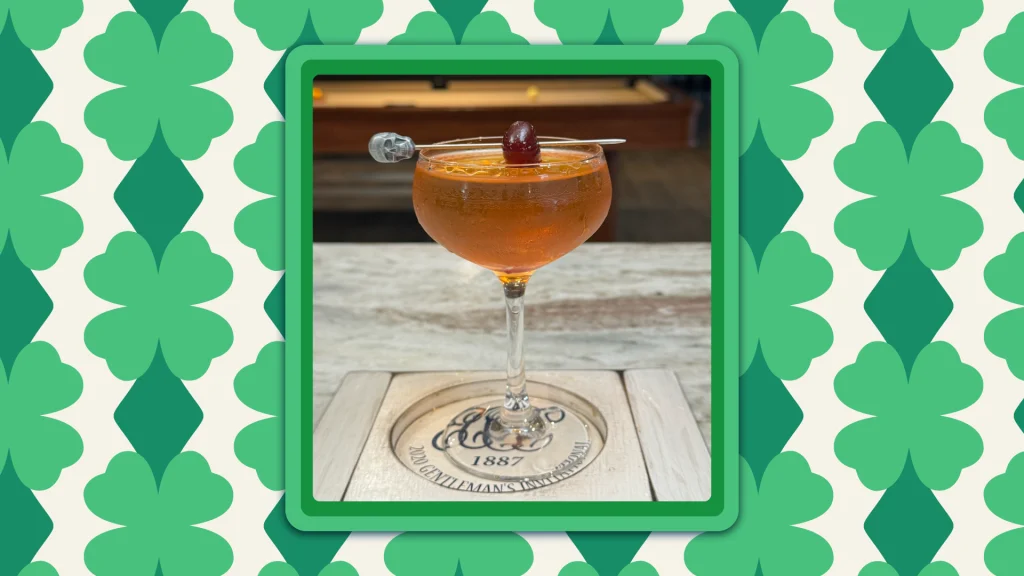 A martini-style glass with The Dubliner cocktail and a cherry on top, on a marble bar.